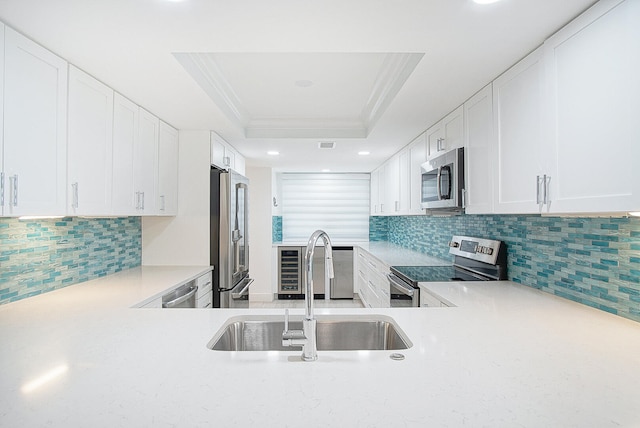 kitchen featuring sink, a raised ceiling, tasteful backsplash, white cabinets, and appliances with stainless steel finishes