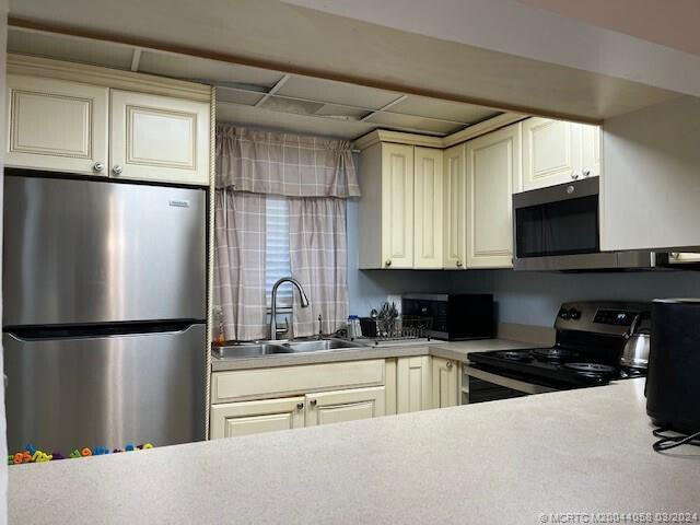 kitchen with cream cabinetry, sink, stainless steel appliances, and a drop ceiling