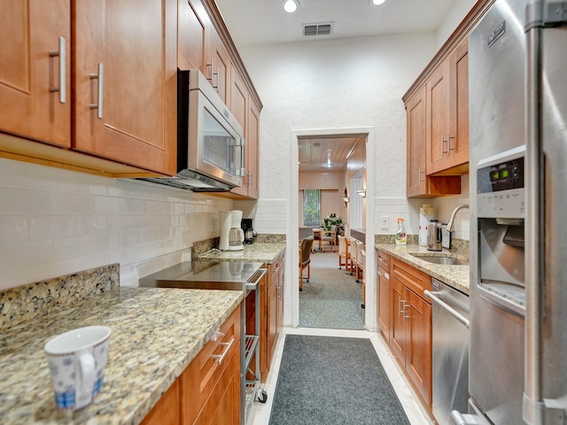 kitchen with stainless steel appliances, sink, light colored carpet, and light stone countertops