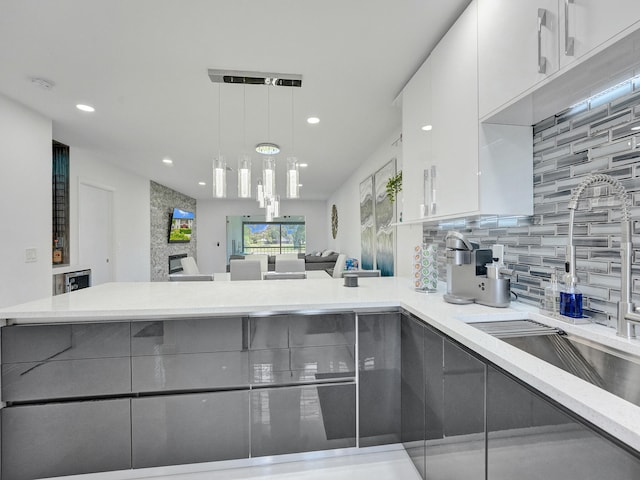 kitchen featuring white cabinetry, sink, decorative light fixtures, a fireplace, and decorative backsplash