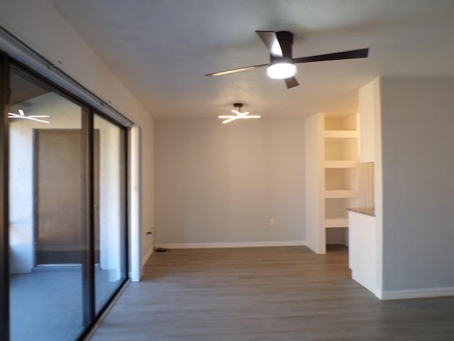 spare room with ceiling fan, built in shelves, and wood-type flooring