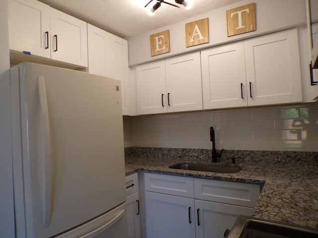 kitchen with dark stone counters, white cabinets, backsplash, sink, and white fridge