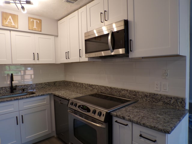 kitchen with dark stone counters, tasteful backsplash, sink, white cabinets, and appliances with stainless steel finishes