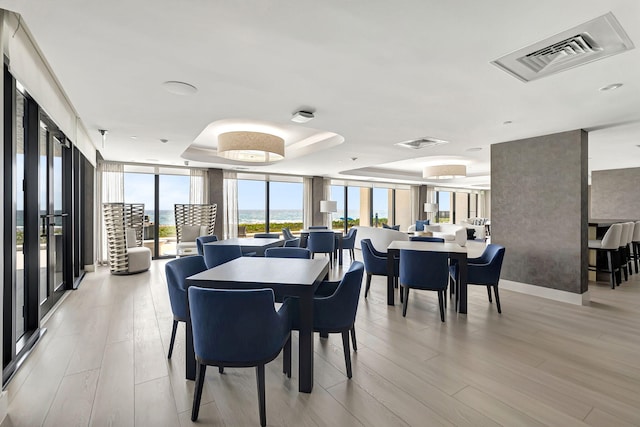 dining area featuring floor to ceiling windows, a raised ceiling, and light hardwood / wood-style floors