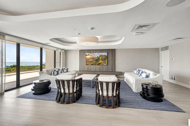 living room with floor to ceiling windows, light wood-type flooring, a water view, and a raised ceiling