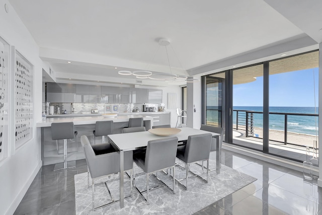 dining room featuring a water view, light tile floors, and a view of the beach