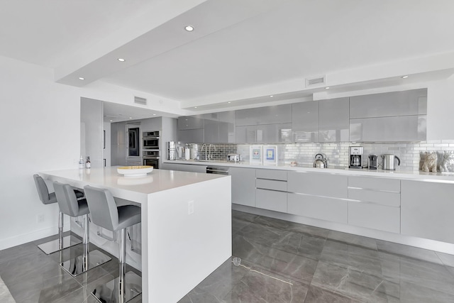 kitchen featuring appliances with stainless steel finishes, tasteful backsplash, dark tile flooring, a kitchen breakfast bar, and gray cabinetry