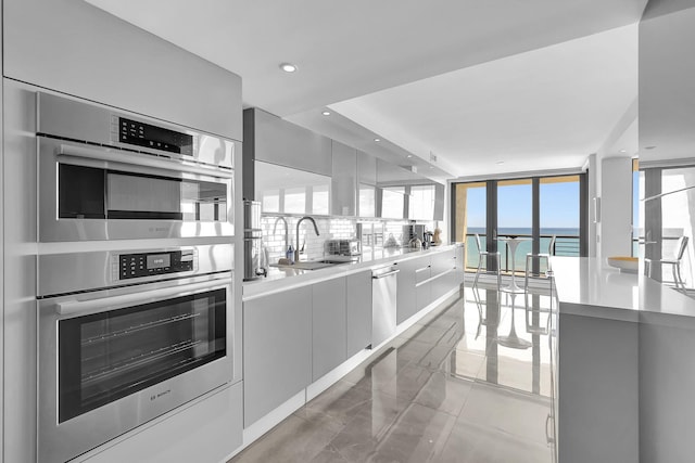 kitchen with light tile flooring, backsplash, appliances with stainless steel finishes, sink, and floor to ceiling windows