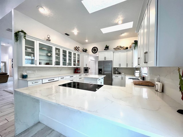 kitchen with light stone countertops, kitchen peninsula, appliances with stainless steel finishes, and a skylight