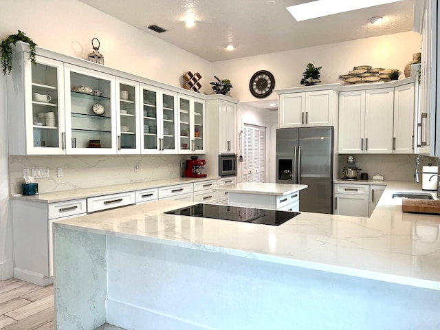 kitchen with kitchen peninsula, appliances with stainless steel finishes, light stone counters, sink, and white cabinets