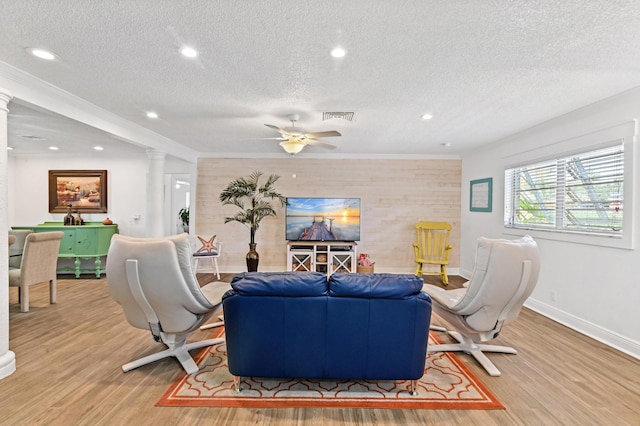 living room featuring decorative columns, ceiling fan, a textured ceiling, and light wood-type flooring