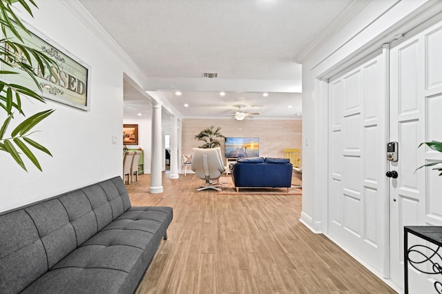 living room with decorative columns, light hardwood / wood-style flooring, ceiling fan, and ornamental molding