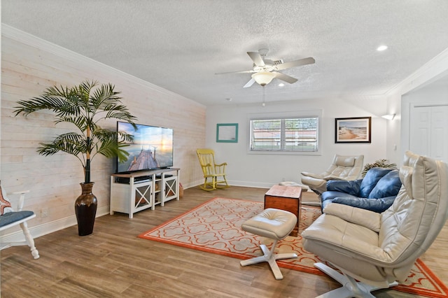 living room featuring ornamental molding, a textured ceiling, ceiling fan, wooden walls, and hardwood / wood-style floors