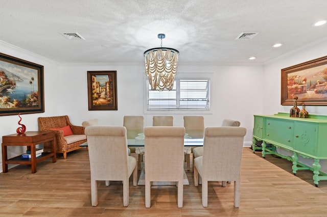 dining space featuring a textured ceiling, light hardwood / wood-style floors, an inviting chandelier, and crown molding