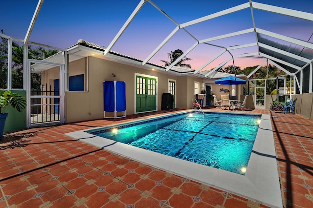 pool at dusk with glass enclosure and a patio