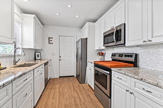 kitchen with sink, light wood-type flooring, appliances with stainless steel finishes, tasteful backsplash, and white cabinetry