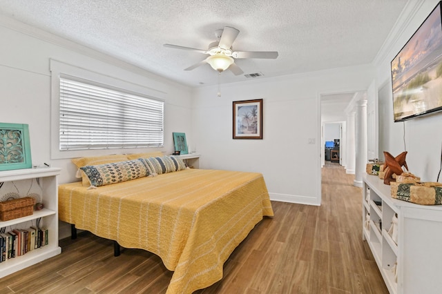 bedroom with hardwood / wood-style floors, a textured ceiling, ceiling fan, and ornamental molding