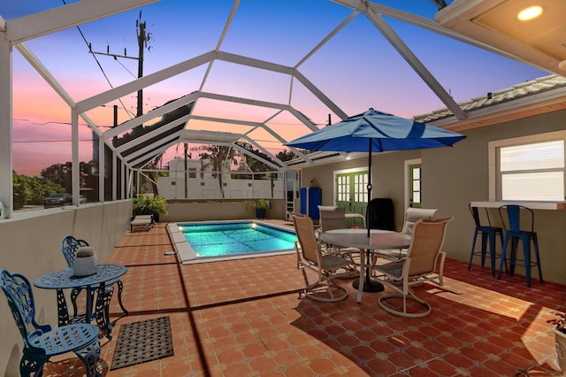 pool at dusk featuring exterior bar, a patio, and glass enclosure