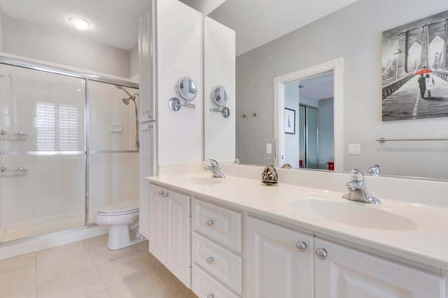 bathroom featuring tile flooring, large vanity, double sink, toilet, and a shower with door