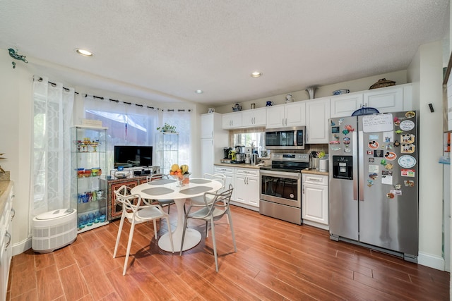 kitchen featuring a textured ceiling, white cabinetry, light hardwood / wood-style flooring, and stainless steel appliances