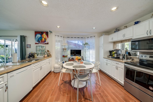 kitchen with white cabinetry, stainless steel appliances, light wood-type flooring, and a healthy amount of sunlight