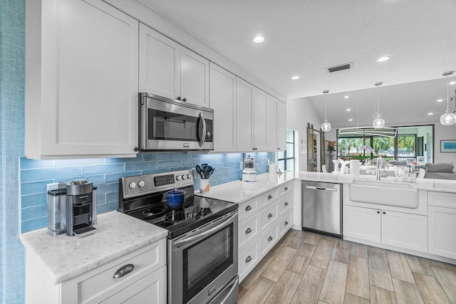 kitchen with white cabinets, kitchen peninsula, appliances with stainless steel finishes, and decorative light fixtures