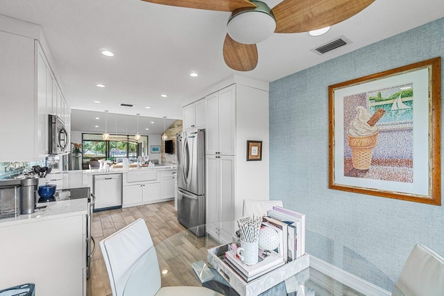 kitchen with white cabinetry, appliances with stainless steel finishes, hanging light fixtures, ceiling fan, and light hardwood / wood-style flooring