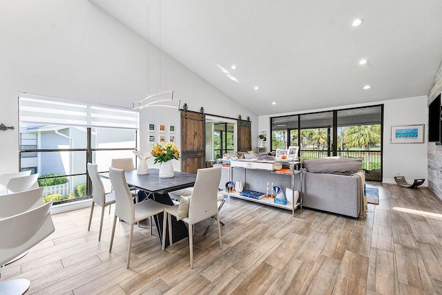 dining room featuring high vaulted ceiling, a barn door, a healthy amount of sunlight, and light hardwood / wood-style flooring