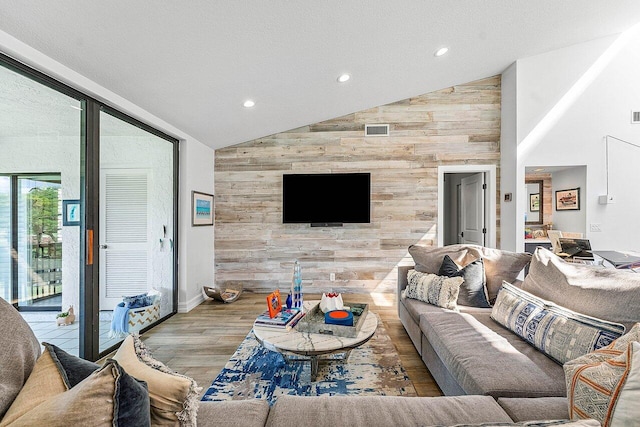 living room with high vaulted ceiling, wood walls, a textured ceiling, and light hardwood / wood-style floors