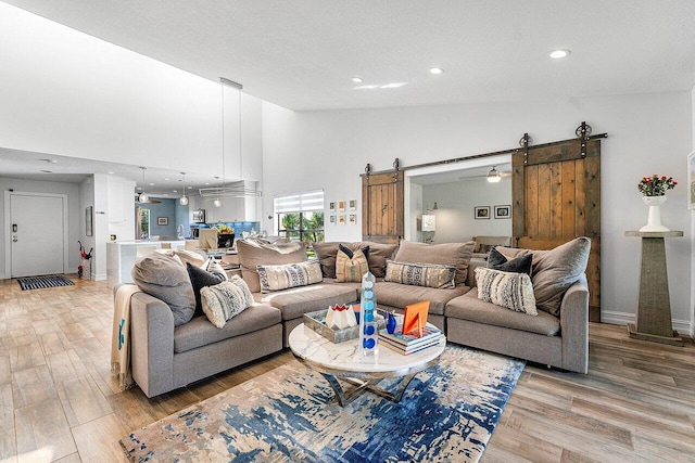 living room with high vaulted ceiling, a barn door, hardwood / wood-style flooring, and ceiling fan