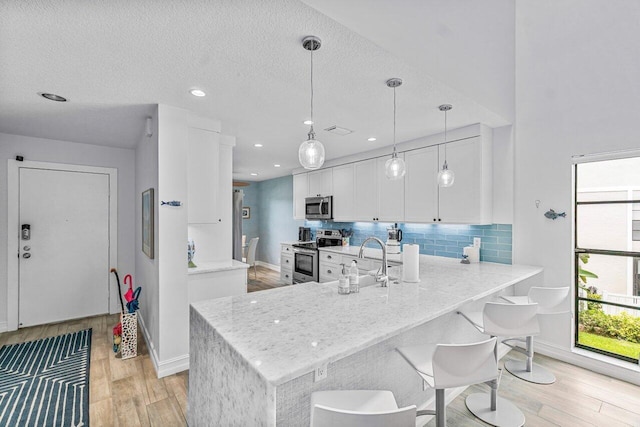 kitchen featuring white cabinetry, kitchen peninsula, appliances with stainless steel finishes, hanging light fixtures, and light wood-type flooring