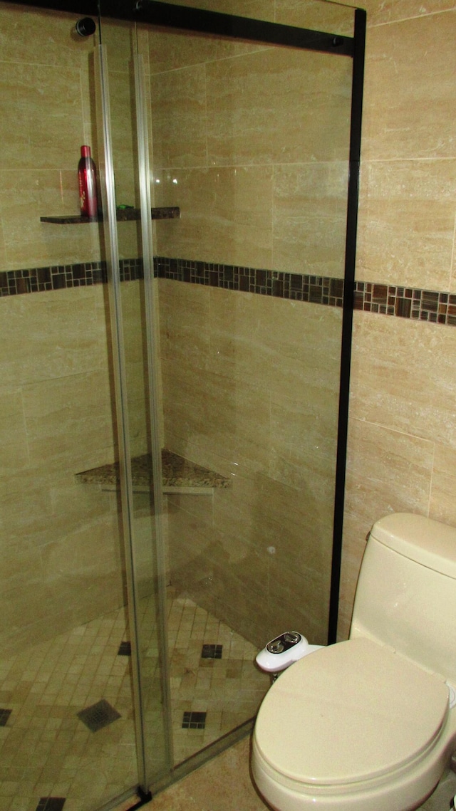 bathroom featuring a shower with door, tile walls, and toilet