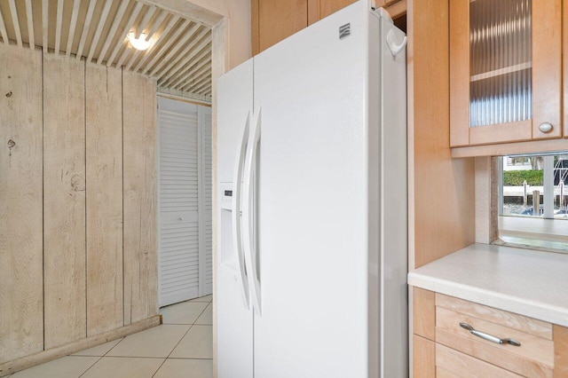 kitchen with light tile patterned floors, white fridge with ice dispenser, and wooden walls