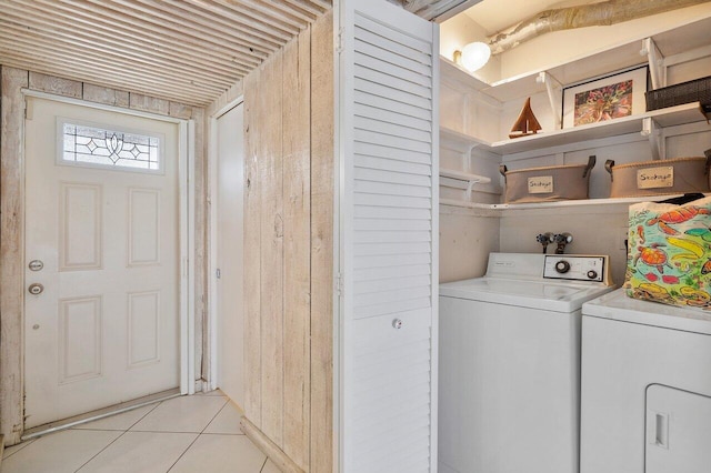 laundry room with washing machine and dryer, light tile patterned flooring, and wood walls