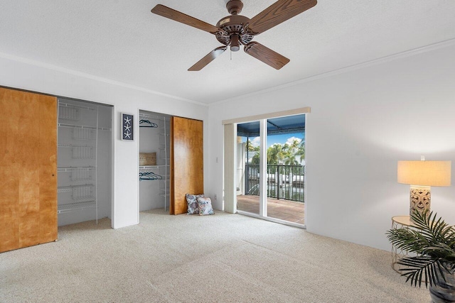 unfurnished bedroom with two closets, ceiling fan, carpet floors, access to outside, and crown molding