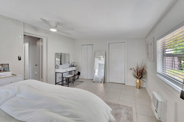 bedroom featuring multiple closets, a wall mounted air conditioner, ceiling fan, and light tile flooring