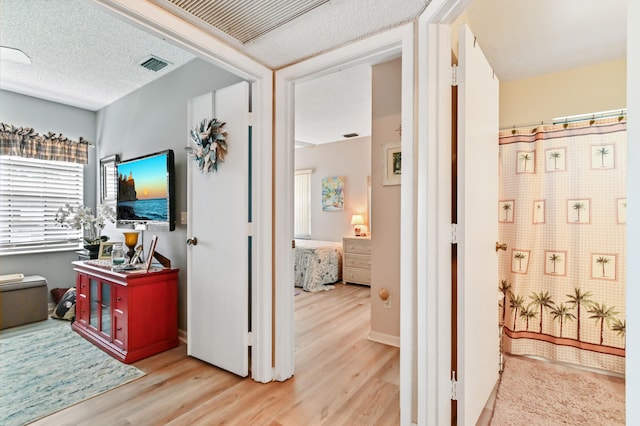 hallway with light hardwood / wood-style floors and a textured ceiling