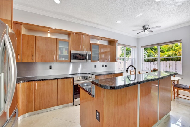 kitchen with light tile flooring, appliances with stainless steel finishes, ceiling fan, and an island with sink