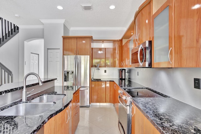 kitchen with sink, light tile flooring, stainless steel appliances, ornamental molding, and dark stone countertops