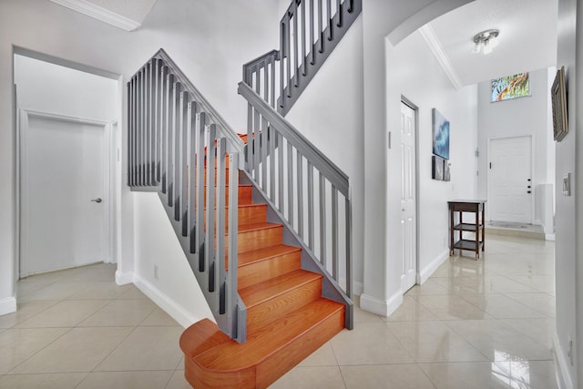 staircase with a high ceiling, crown molding, and light tile floors