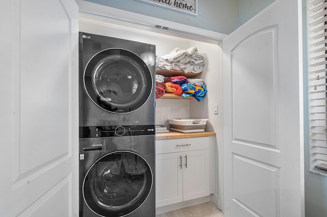 clothes washing area with stacked washing maching and dryer and cabinets