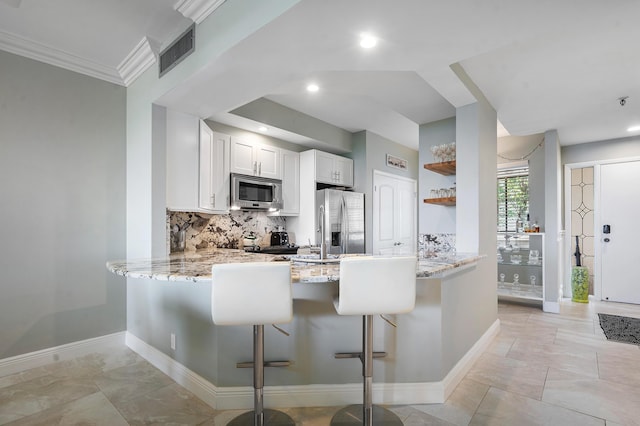 kitchen featuring a breakfast bar area, stainless steel appliances, white cabinets, backsplash, and kitchen peninsula