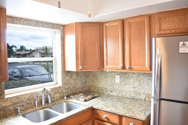 kitchen featuring light stone counters, tasteful backsplash, stainless steel refrigerator, and sink