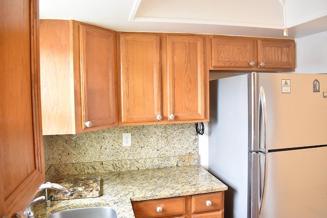 kitchen with light stone counters, stainless steel refrigerator, sink, and decorative backsplash