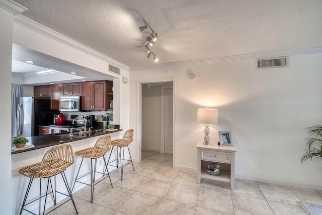 kitchen featuring stainless steel appliances, kitchen peninsula, crown molding, a textured ceiling, and a breakfast bar