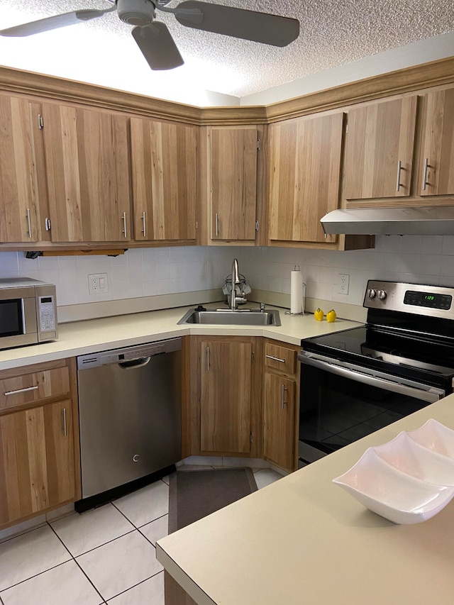 kitchen featuring appliances with stainless steel finishes, light tile patterned floors, a textured ceiling, ceiling fan, and sink