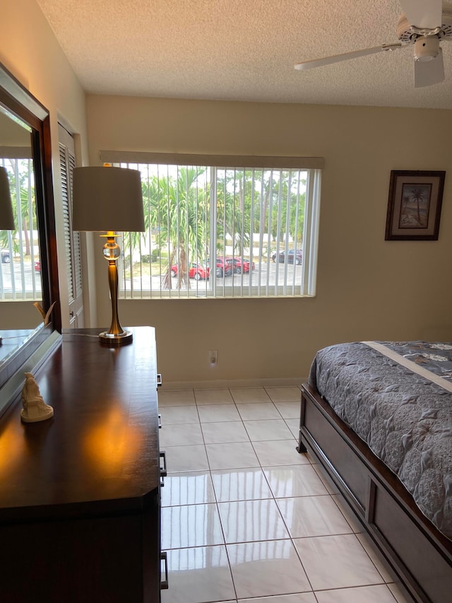 bedroom with ceiling fan, multiple windows, light tile patterned flooring, and a textured ceiling