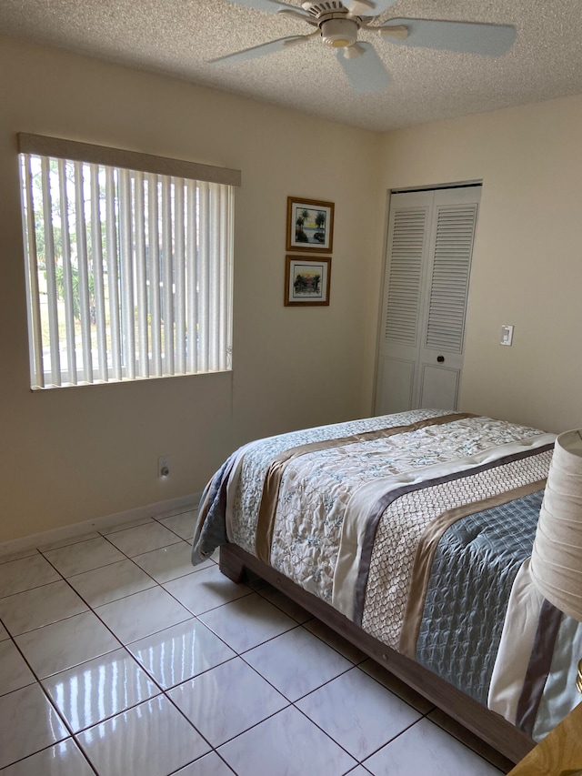 bedroom featuring a closet, ceiling fan, light tile patterned flooring, and a textured ceiling