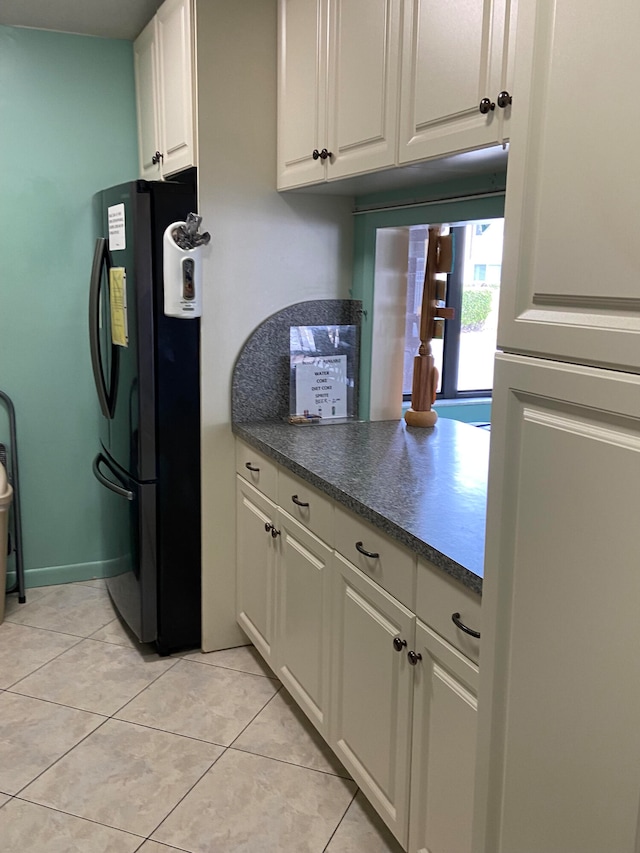 kitchen with light tile patterned floors, white cabinets, and black refrigerator