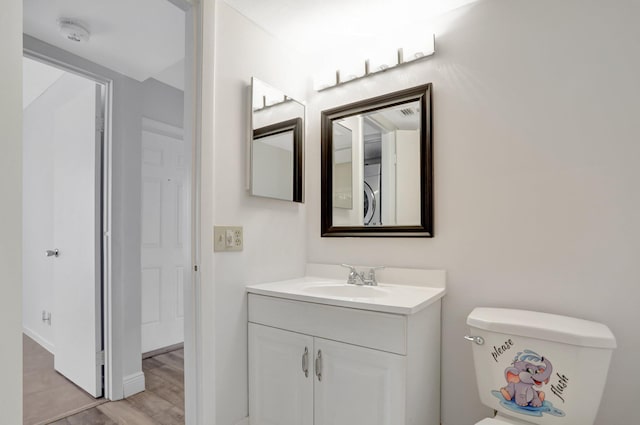 bathroom with hardwood / wood-style floors, toilet, vanity with extensive cabinet space, and washer / dryer